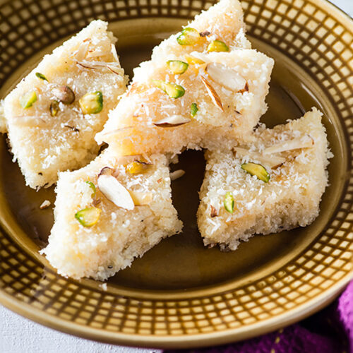 Coconut burfi is tasty traditional Indian sweet that can be made in minutes. Traditionally coconut burfi is made with milk but this is coconut burfi recipe with Milk powder, desiccated coconut, and sugar. An instant Indian Mithai that can be made in minutes.