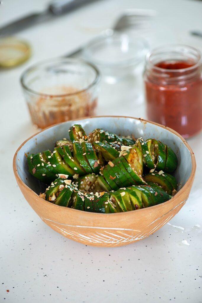 Asian cucumber salad with accordion cut cucumbers, sesame seeds and chili flakes in a clay bowl